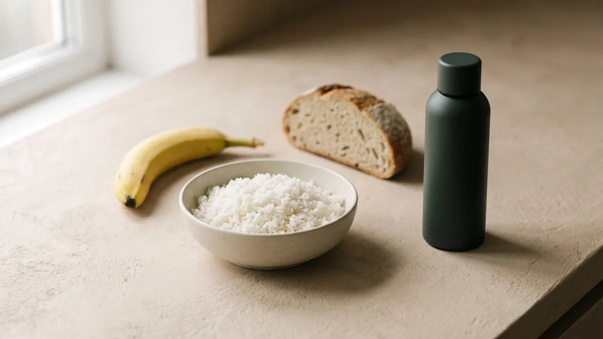 Un bol de riz blanc, une banane, un morceau de pain et une gourde mate vert foncé sans marque, sur un plan de travail clair.